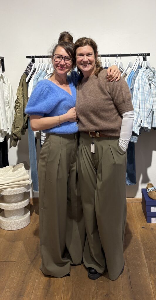 Zwei Frauen nach einem erfolgreichen Personal Shopping in München mit modernen Outfits aus weiter Stoffhose und hochwertigem Strick – Beispiel für individuelle Stilberatung und zeitlose Mode.