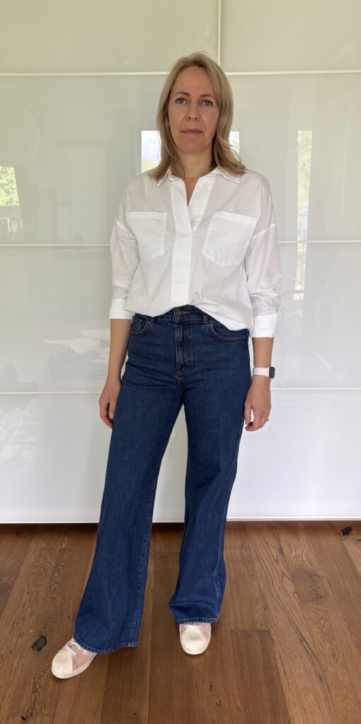 Zeitloses Outfit für Frauen ab 40 mit weißer Hemdbluse, dunkelblauer Wide-Leg-Jeans und weißen Sneakern – modernes Beispiel für stilvolle Basics und eine vielseitige Garderobe.