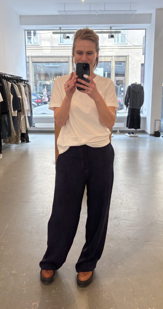 Personal Stylistin Heide von STYLEFINDS trägt ein weißes Basic-T-Shirt, eine dunkelblaue Stoffhose und braune Loafer – Beispiel für hochwertige Basics und eine moderne Garderobe.